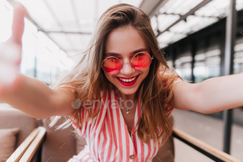 Good-humoured female model with straight hair making selfie with smile. Indoor shot of laughing ecs / Photodune