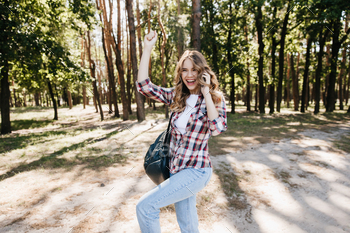 Spectacular young lady in jeans dancing in summer forest. Carefree girl with backpack fooling aroun / Photodune