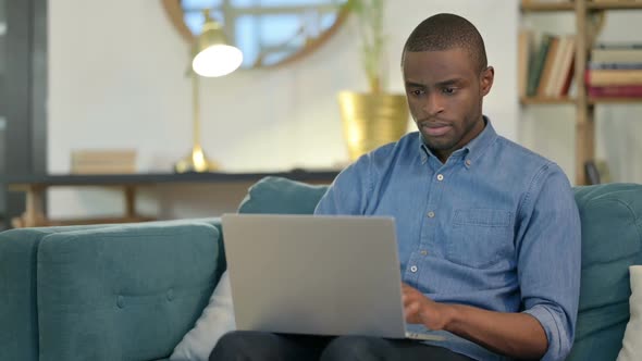 Beautiful Young African Man Using Laptop on Sofa