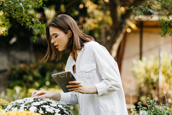 Interested girl in oversize shirt looking at flowers. Short-haired woman holding digital tablet in / Photodune