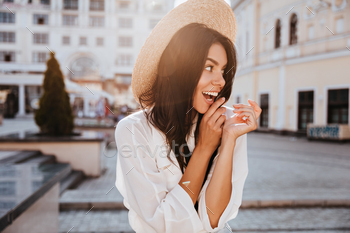 Excited black-haired girl in straw hat posing on urban background. Outdoor shot of laughing good-hu / Photodune