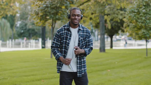 African American Stylish Cheerful Carefree Man Young Happy Guy in Park Wears Headphones Uses Mobile