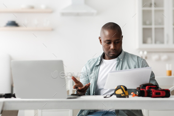  reading manual and does not understand what to do, sitting at table with tools and laptop in kitchen interior. Home repairs concept