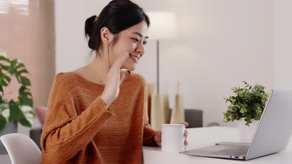 Young modern Asian woman works from home with laptop computer in living room.