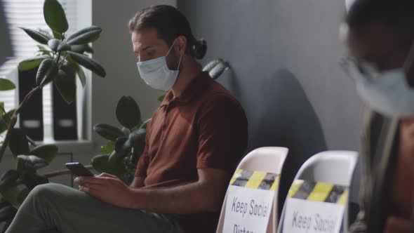 Diverse Men in Masks Using Smartphones and Waiting for Job Interview