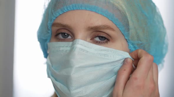 Sad and Tired Young Female Doctor or Nurse in Face Protective Medical Mask and Gloves Taking Mask