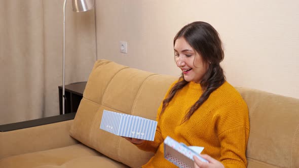 Young Woman Rejoices Opening a Gift While Sitting on the Sofa