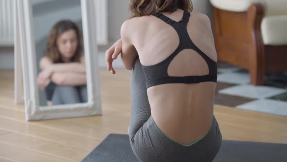 Back View of Extremely Slim Young Woman Sitting on Exercise Mat Hugging Knees