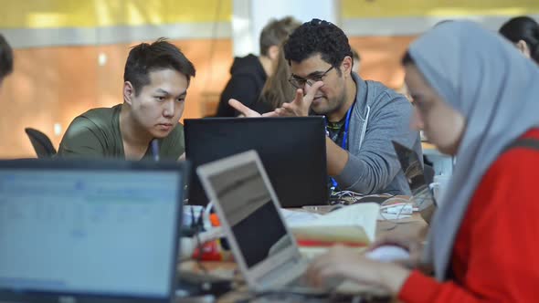 Young Multiethnic Students Communicate Actively at Table with Laptops in University Irrl