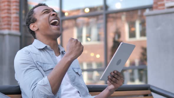 Sitting Outdoor African Man Cheering Success on Tablet