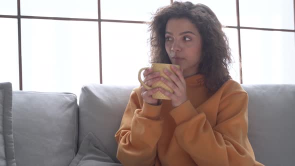 Happy Young Hispanic Woman Relaxing on Comfortable Sofa Drinking Tea at Home