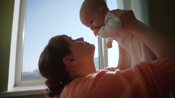 Happy Young Mother Throws Her Baby Up and Kisses