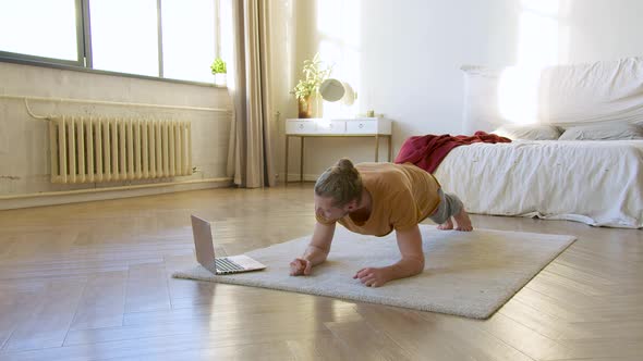 Young Man in Front of Laptop Monitor Doing the Plank Exercise