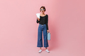 Surprised girl in jeans holding tickets on pink background. Excited woman with suitcase waiting for - PhotoDune Item for Sale