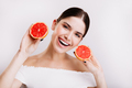 Snapshot of young gray-eyed girl with snow-white smile showing juicy and healthy grapefruits on whi - PhotoDune Item for Sale