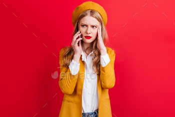 phone. Studio shot of caucasian girl in jacket holding smartphone on red background.
