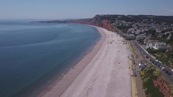 Flying over the ocean while the cars are driving on the road right next to the beach. English beach