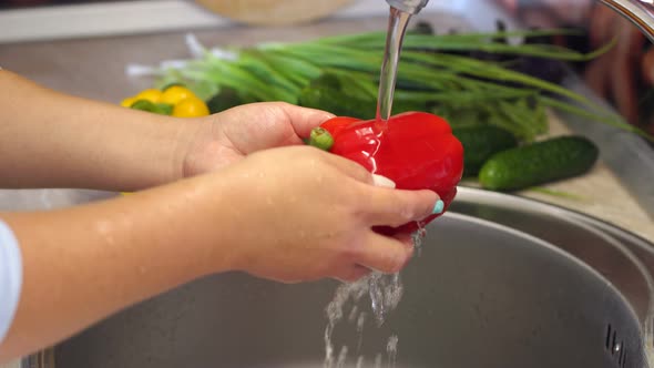 Closeup of a Young Girl Washing Red Bell Peppers at Home in the Kitchen