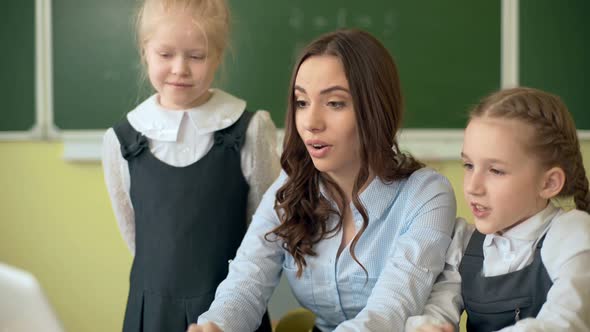 Happy Teacher Using Laptop with Pupils in the Classroom