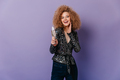 Portrait of blonde curly girl in shiny black blouse laughing and holding glass of white wine on pur - PhotoDune Item for Sale