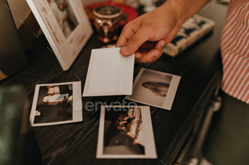 Shot of mans hand putting photo on wooden coffee table to other memorable pictures / Photodune, Misc