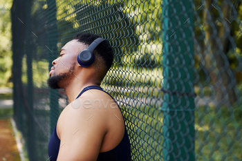ワイヤレス ヘッドフォンのアフリカ系アメリカ人の男は、スポーツ コートの金属メッシュに寄りかかっています。 / Photodune, Misc