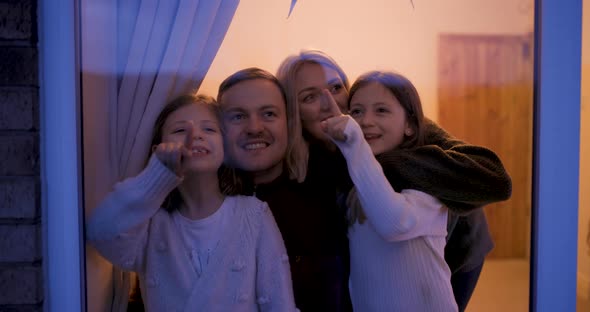 Happy family at home looking out of the window at night and having fun