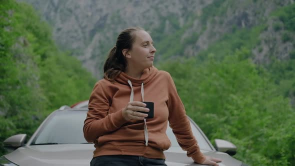 Woman traveler drinking hot tea  and looking at mounain view during a car summer trip