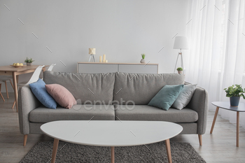 gn. Gray sofa with colored pillows, carpet, table, window with curtain on white wall background, in living room interior, free space, nobody, indoor
