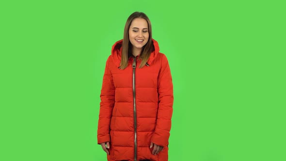 Lovely Girl in a Red Down Jacket Is Coquettishly Smiling While Looking at Camera