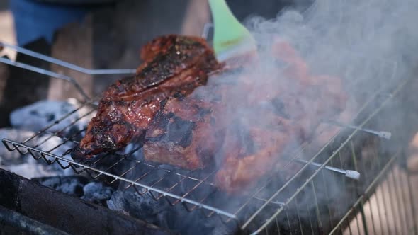 Delicious Beef or Pork Ribs Frying on a Charcoal Grill Being Covered with Red Gravy Sauce Brush