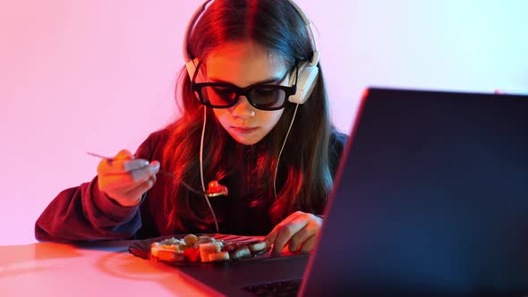 Girl in Glasses for 3D and Headphones Watches Movie on Laptop and Eats