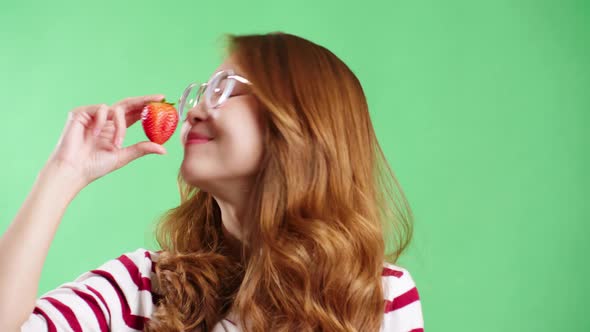 Young woman enjoying strawberry in studio with green screen chroma key background.