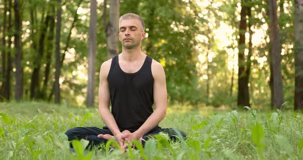 Young Man Sitting on Lawn Doing Meditation in City Park