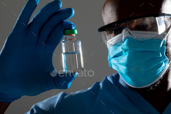 Close up of african american male health worker wearing face mask holding covid-19 vaccine bottle / Photodune, Misc