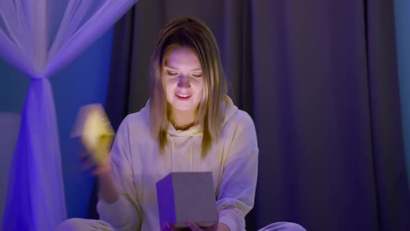 Surprised Smiling Woman Opens Golden Glitter Gift Box with Magic Light Inside 8K