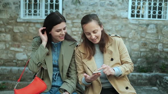 Two woman in coats outdoors in spring time looking in to a smartphone