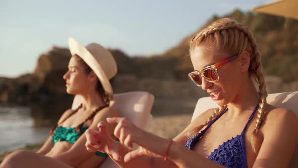 Two Young Beautiful Girls Laughing at the Sea Side Sitting in Chaise Lounges