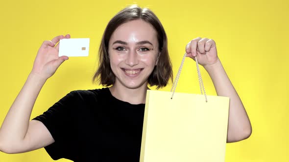 Smiling young woman holding credit card on yellow background