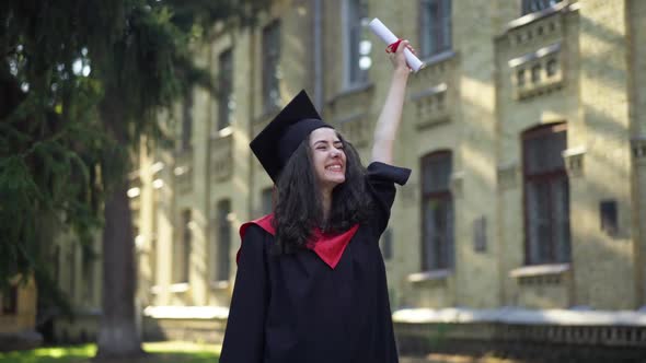 Cheerful Graduate Stretching Hand with Diploma Up Smiling Looking Away Standing Outdoors