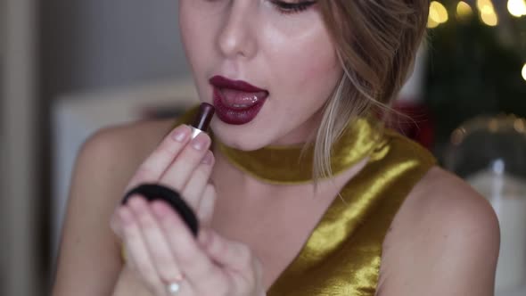 young beautiful woman applying cosmetics near Holiday decorated mirror at home.