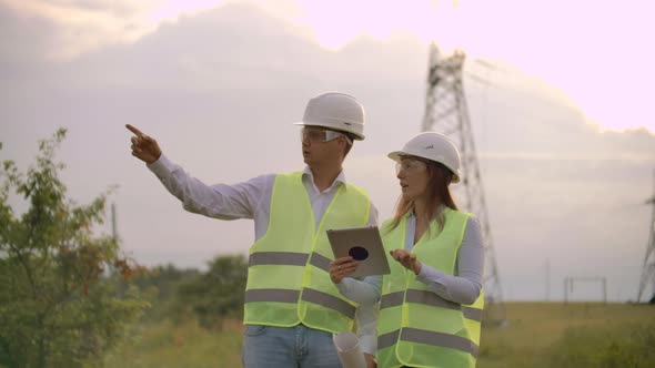 Engineers in Uniform Working with a Laptop Near Transmission Lines