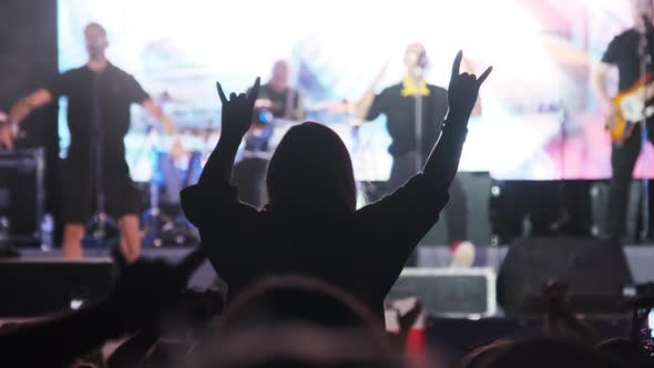 Silhouette of Woman in Crowd at Rock Concert Showing Sign Devil's Horns Gesture