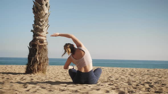 Woman in Sportswear Sits on the Beach at Sunny Day Enjoying Life and Doing Yoga and Stretching