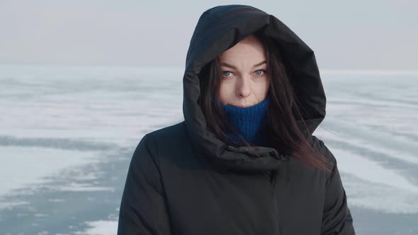 Young Woman in Warm Down Jacket with a Hood in Cold Winter on Snowy Arctic Background