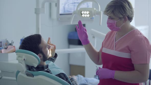 Dentist in Medical Mask and Gloves Checking Condition of Her Patient Using Gestures