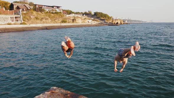 Young Woman and Man Jumping From a Pier Into the Sea During Beautiful Sunrise Super Slow Motion