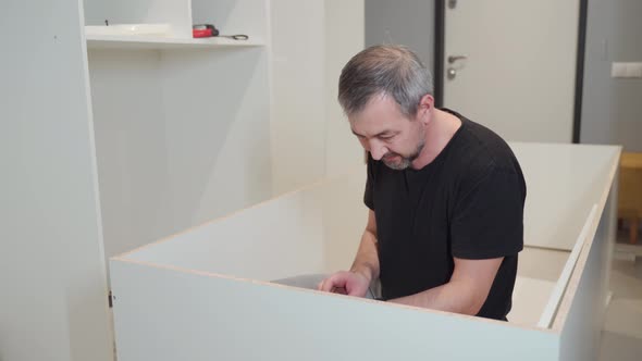 A Man is Screwing a Screw Into the Cabinet Body with a Screwdriver