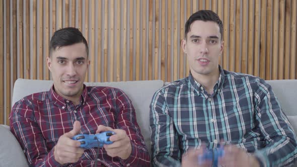 Positive Caucasian Twin Brothers Playing Video Game, Guy in Blue Shirt Looses, His Sibling in Red