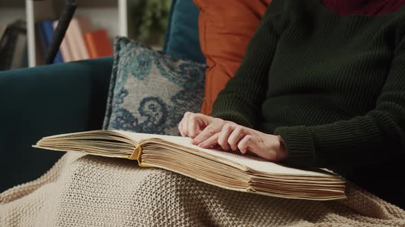 Blind Woman Reading Braille Book Using Fingers Sitting on Sofa in Living Room Poorly Seeing Female